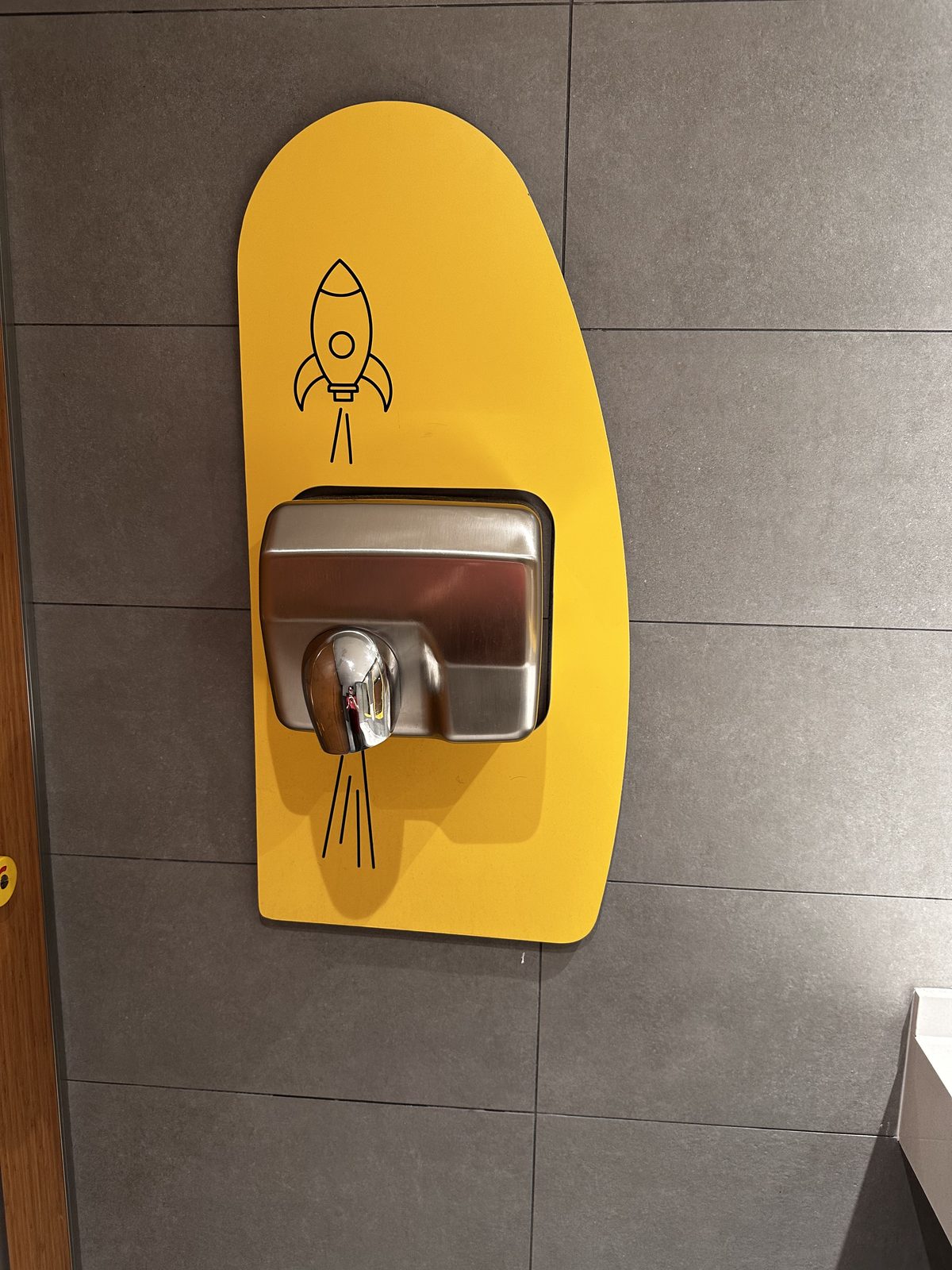 A wall-mounted hand dryer on a yellow decal shaped like a rocket's exhaust trail