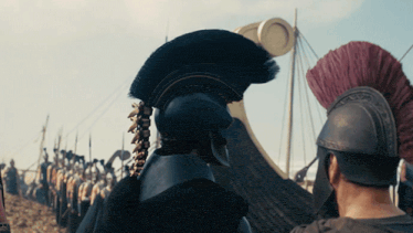 Two helmeted warriors face off on a beach lined with ships, Agamemnon's face mostly hidden by his helmet
